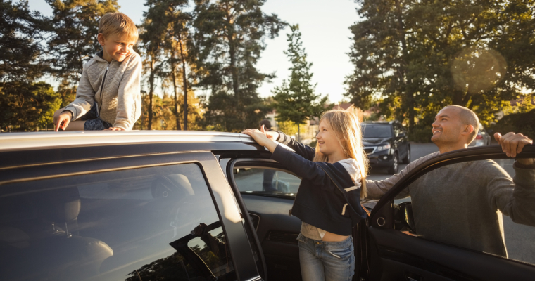 a woman and man lean on an open car door while their son looks on.