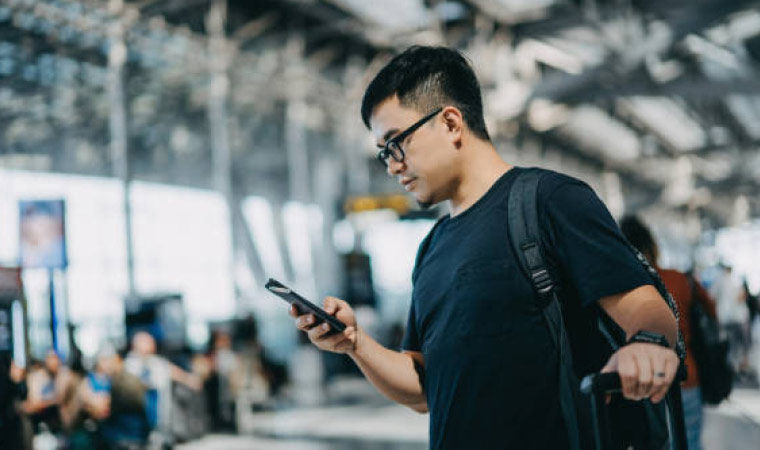 A man standing in an airport looking at his phone. 