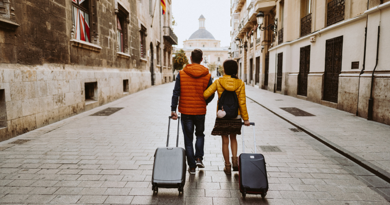 A couple walking through a European street with their suitcases in tow