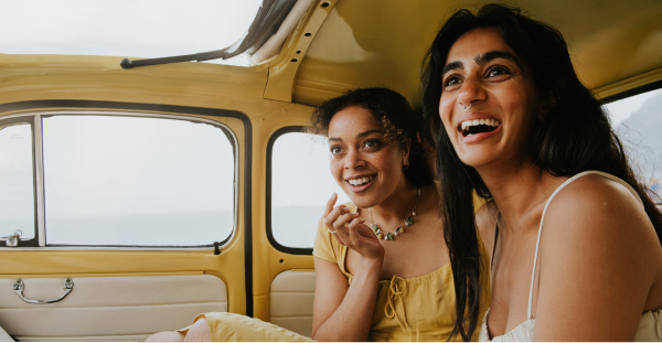 Two happy woman in the backseat of a vintage yellow fiat 500