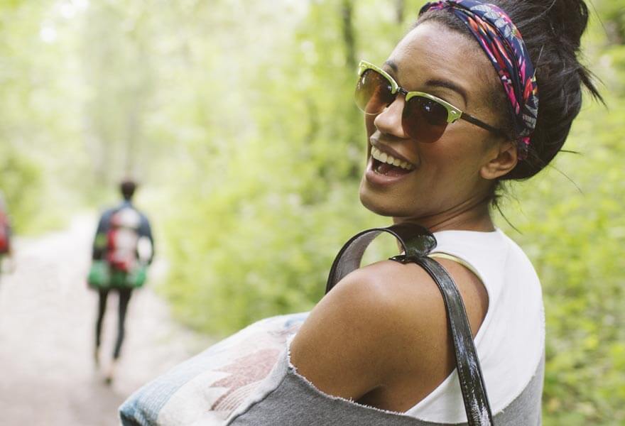 A smiling woman wearing a bandana and carrying a bag on a hike