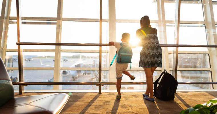 A woman and child looking out the window at an airport