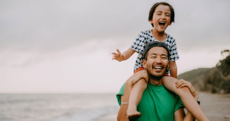 A child on their fathers shoulders on the beach