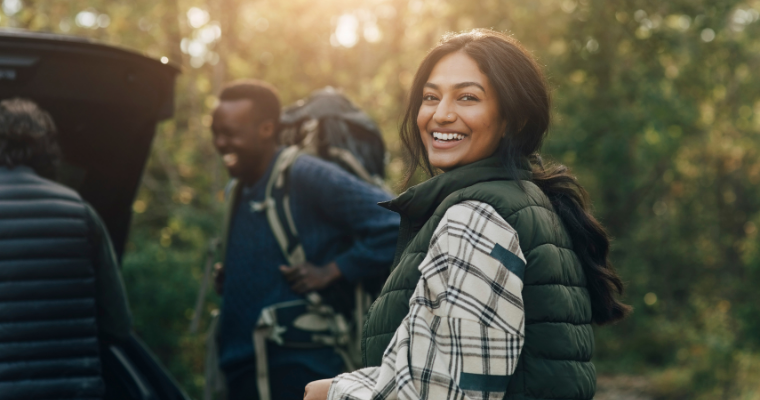 A woman on a hiking trip smiling, with people wearing hiking clothes and backpacks around her