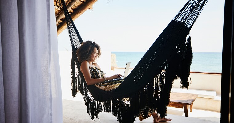 A digital nomad working on a laptop while relaxing in a hammock next to the ocean